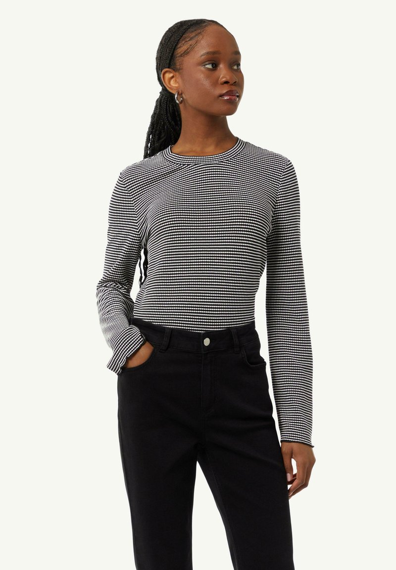 Long-sleeve top in black and white checkered pattern, featuring a round neckline and fitted design. Paired with high-waisted black pants.