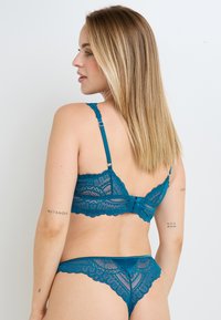 Set di reggiseno e perizoma in pizzo turchese, con bordi a scallop, spalline regolabili e un motivo floreale. Texture morbida con un design classico.