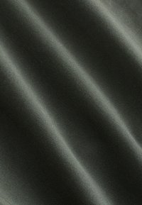 Gros plan d'un tissu vert foncé avec un tissage sergé diagonal fin et des plis doux créant des ombres subtiles.
