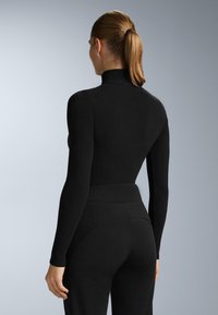 Fekete garbós body hosszú ujjakkal, sima textúrával, testhez simuló fazonnal, varrásmentes kialakítással, magas derekú fekete nadrággal párosítva.