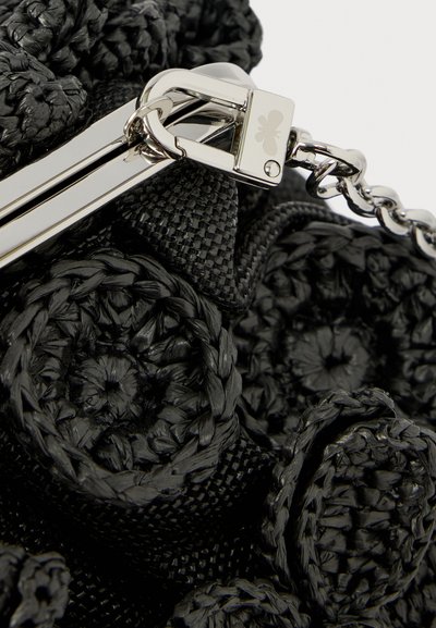 Κοντινό πλάνο μαύρου υφασμάτινου υλικού με κυκλικά μοτίβα και ασημένιο μεταλλικό κούμπωμα προσαρτημένο σε αλυσίδα.