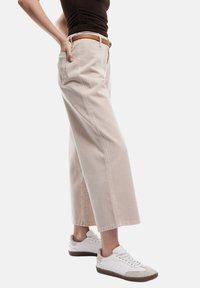 Beige leveled pantsi širšega kroja z stranskimi žepi, narejeni iz mešanice bombaža. V kombinaciji z belimi supergami, ki imajo svetlo sivo akcentno barvo in rjave podplate.