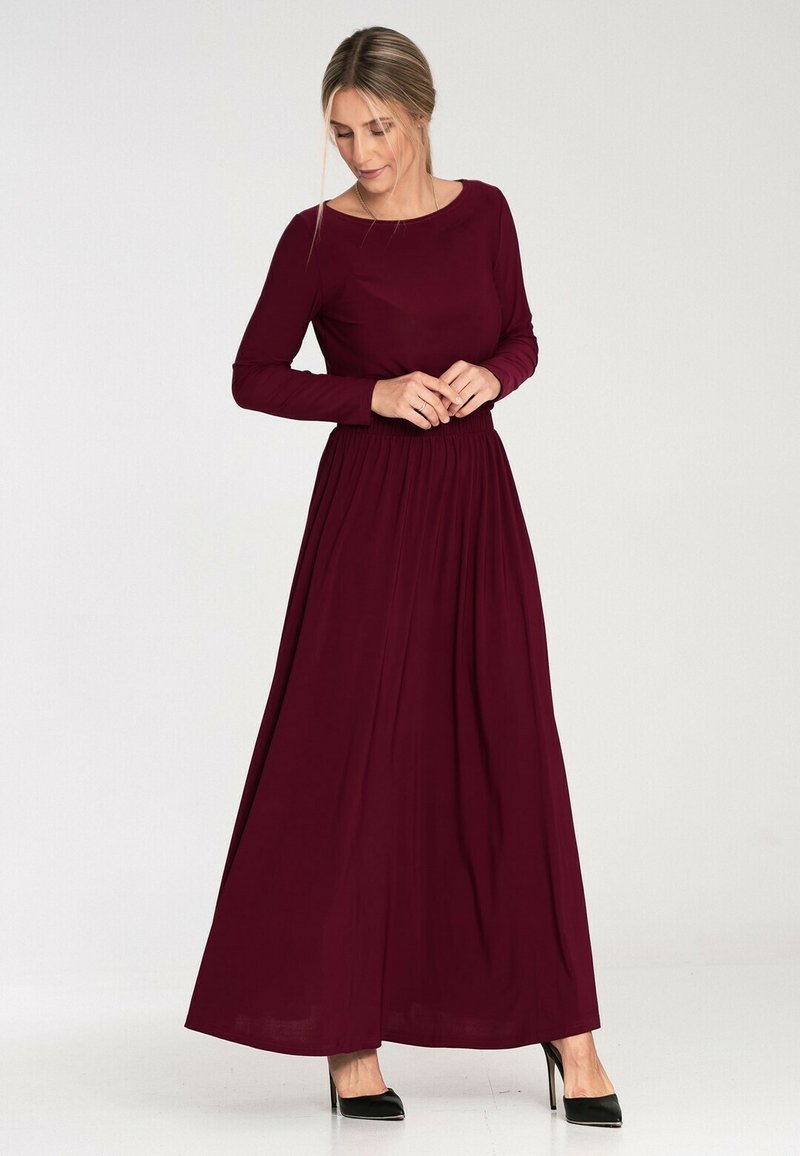 Długa burgundowa sukienka z długimi rękawami, okrągłym dekoltem, marszczonym w pasie, zwiewnym dołem i gładką fakturą. Noszona z czarnymi szpilkami.