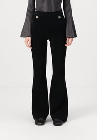Pantalons évasés noirs avec une texture lisse, taille haute et deux poches avant avec des accents de boutons dorés.