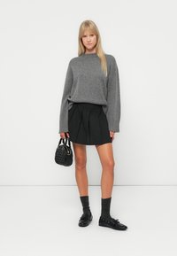 Grijze gebreide trui, zwarte geplooide rok, zwarte tas, grijze sokken en zwarte schoenen. Glad materiaal, casual ontwerp en gelaagde texturen.