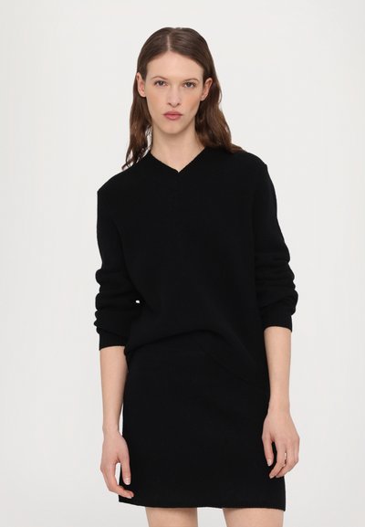Schwarzer Pullover mit V-Ausschnitt, langen Ärmeln und lockerer Passform, kombiniert mit einem passenden schwarzen Rock. Strukturierter Strickstoff.