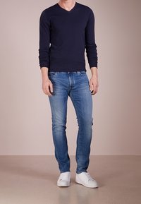 Pull à manches longues bleu marine avec col en V, associé à un jean bleu clair et à des baskets blanches. Le pull est ajusté, avec une texture lisse.