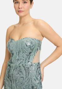 Halsloze, mintgroene jurk met verfijnde bead- en paillettendetails, voorzien van doorzichtige zijpanelen en een aansluitende silhout.
