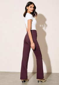 Pantaloni burdundii evazați din denim, cu talie medie și buzunare la spate, asociați cu un tricou alb ajustat și pantofi cu un model.