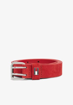 Rode suède riem met zilveren dubbele gesp en klein Tommy Jeans-logo op de riemlus, opgerold op een witte achtergrond.