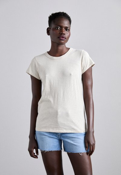 T-shirt à manches courtes et col rond en beige clair, fabriqué dans un tissu doux ; associé à un short en denim bleu clair avec des ourlets effilochés.