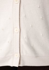 Lichtbeige cardigan met een zachte textuur, voorzien van kleine parelaccenten en witte knopen aan de voorkant.
