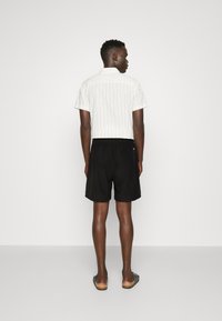 White striped short-sleeve shirt with a collar, paired with black elastic-waist shorts. Model wearing slide sandals.