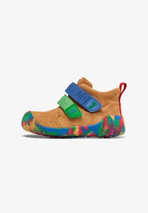 Chaussure en suède marron avec deux bandeaux auto-agrippants en bleu et vert. La semelle texturée présente un motif floral multicolore. Tirant rouge sur le talon.