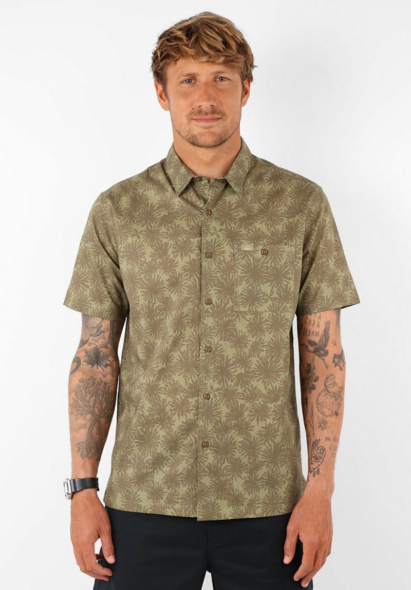 Chemise à manches courtes, de couleur olive, à boutons, avec un motif répétitif de feuilles de palmier, dotée d'une poche poitrine et de boutons marron.