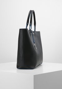 Czarna skórzana torba tote o wyrazistej formie, gładkiej fakturze, kontrastowych niebieskich akcentach na uchwytach oraz ozdobnej srebrnej zawieszce.