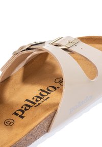 Sandalo beige con sottopiede in sughero, dotato di due cinturini regolabili con fibbie metalliche. Soletta testurizzata con il marchio "palado" ben visibile.