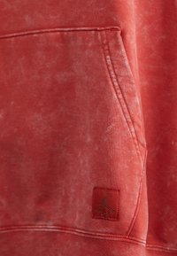 Sudadera roja con textura desgastada. Cuenta con un bolsillo tipo canguro y un pequeño logo de Jordan bordado en el frente.