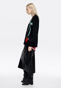 Czarny dziergany sweter z wielokolorowym abstrakcyjnym wzorem, noszony na czerwonym topie. Zestawiony z błyszczącą czarną skórzaną spódnicą i czarnymi kozakami sięgającymi do kolan.