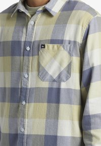 Flanellen shirt met een ruitenpatroon in tinten geel, blauw en grijs. Knopsluiting aan de voorkant met een enkele opgestikte zak en zachte textuur.