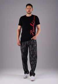 Schwarzes T-Shirt mit rotem Aufdruck und eng anliegende gemusterte Hosen in Schwarz- und Grautönen, kombiniert mit weißen Sneakers.