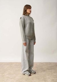 Maglione grigio chiaro a maglia con maniche lunghe, abbinato a jeans ampi grigi chiari e sneakers con motivo. Design semplice e testurizzato.