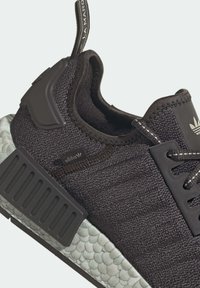 Närbild av svart Adidas-sko med texturerad vit sula, stickad ovandel och ett märkt dragflik på hälen.