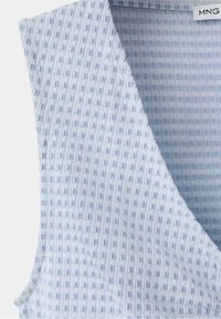 Haut sans manches bleu clair en tissu à texture gaufrée avec col en V, montrant une partie de l’étiquette de la marque à l’intérieur.