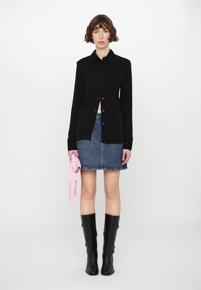Svart langermet skjorte med knapper, denimskjørt, høye svarte støvler, og et rosa tilbehør i hånden. Minimalistisk design, uformell stil.