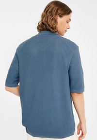 Blå kortärmad polo med en texturerad stickad mönster. Ribbad krage och ärmslut. Rak nederkant med sidoklintar för ökad komfort.