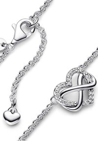 Srebrna zapestnica s povezavo v obliki srca, okrašena s prozornimi kristali in majhnim obeskom v obliki srca. Zapiranje na jeklenko.