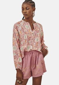 Blusa ligera con estampado floral en tonos rosa y menta, con un cuello delgado, combinada con pantalones cortos rosa con cordón y costuras geométricas.