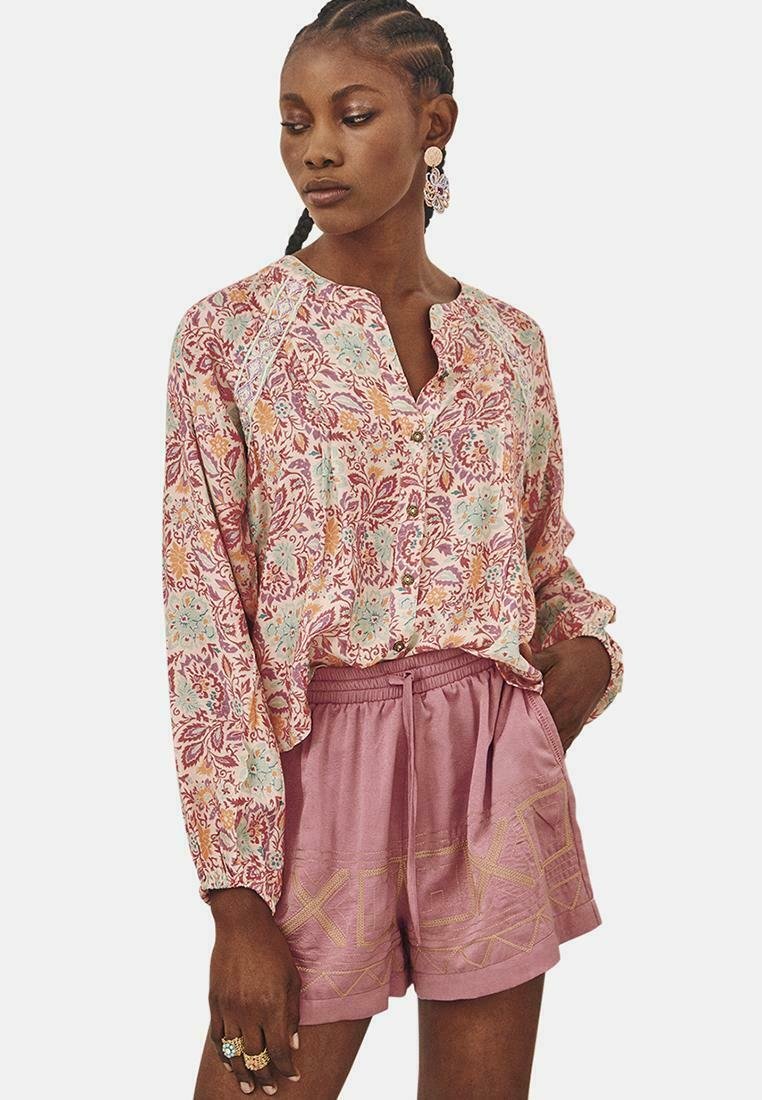 Blusa ligera con estampado floral en tonos rosa y menta, con un cuello delgado, combinada con pantalones cortos rosa con cordón y costuras geométricas.