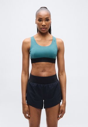 Brassière de sport bleu sarcelle avec larges bretelles et bande inférieure noire, associée à un short de sport noir à coupe décontractée et taille élastique.