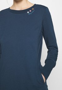 Námořnický bavlněný top s dlouhým rukávem, se kulatým výstřihem, kapsou a dekorativními knoflíky na rameni s vyšitým textem.