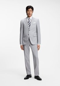 Grauer gestreifter Anzug mit figurbetontem Schnitt, passende Hose, weißes Hemd und gestreifte Krawatte. Schwarze Anzugschuhe vervollständigen das Outfit.