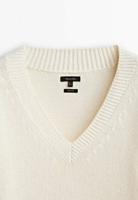 Pull en coton crème à col en V avec motif texturé, col côtelé et corps en tricot plat. Étiquettes visibles à l'intérieur du col.