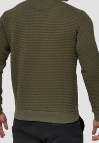 Oliwkowy, teksturowany sweter z haftowanym wzorem, z prążkowanymi mankietami i dołem. W luźnym kroju z okrągłym dekoltem.