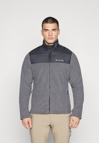 Gray fleece jacket with black padded chest, high collar, full zip, and Columbia logo on the left. Smooth texture with long sleeves.