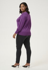 Purple glitter-textured sweater with a relaxed fit and balloon sleeves, paired with black skinny jeans and black heeled mules.