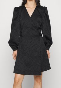 Svart omslagsklänning med V-ringad hals, puffärmar och subtil leopardmönstrad textur. Har sidoknappar och en figursydd midja.