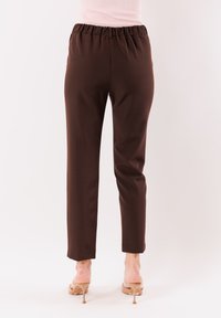 Pantaloni marroni su misura con vita elasticizzata, vestibilità slim e tessuto liscio, che arrivano fino alle caviglie. Nessun motivo visibile o tasche.