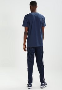 Marinblå t-shirt i bomull med rund hals, ihopparad med marinblå träningsoverallsbyxor med vita sidostråk. Avslappnad sportig klädsel med en slät yta.