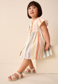 Meerfarben gestreepte jurk van lichtgewicht stof met korte mouwen en knoopdetails. Gecomplementeerd door beige sandalen met bloemrijke borduursels.