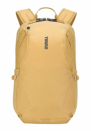 Sac à dos compact jaune moutarde avec bretelles rembourrées, double fermeture éclair supérieure, sangles de réglage latérales et logo "Thule" sur le devant.