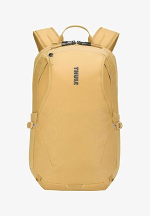 Mochila compacta color mostaza con correas de hombro acolchadas, doble cremallera superior, correas de ajuste lateral y logo "Thule" en la parte frontal.