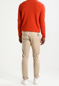 Röd tröja med rundad halsringning, kombinerad med beige smala byxor. Byxorna har en bakficka; vita sneakers fulländar looken.