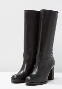 Bottes en cuir noir montant jusqu'au genou avec une finition lisse, un bout arrondi et un talon en bois épais, présentant des coutures minimales et un design sans couture.