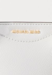 Pochette en cuir blanc avec une surface texturée. Présente un bord surpiqué et un logo doré "MICHAEL KORS" en haut.