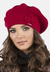Berretto rosso lavorato a maglia con accenti floreali e un piccolo logo metallico. Texture morbida con un design morbido, si adatta aderentemente alla testa.